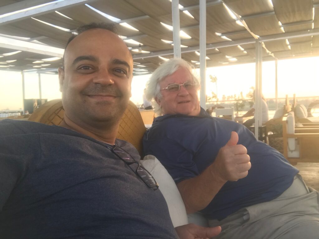 Two men relaxing at an outdoor venue at sunset, one giving a thumbs up